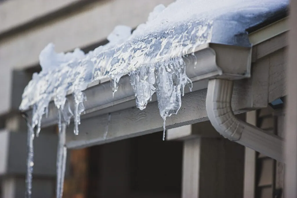 A gutter frozen solid with ice and trapped debris along the edge of a roof in winter