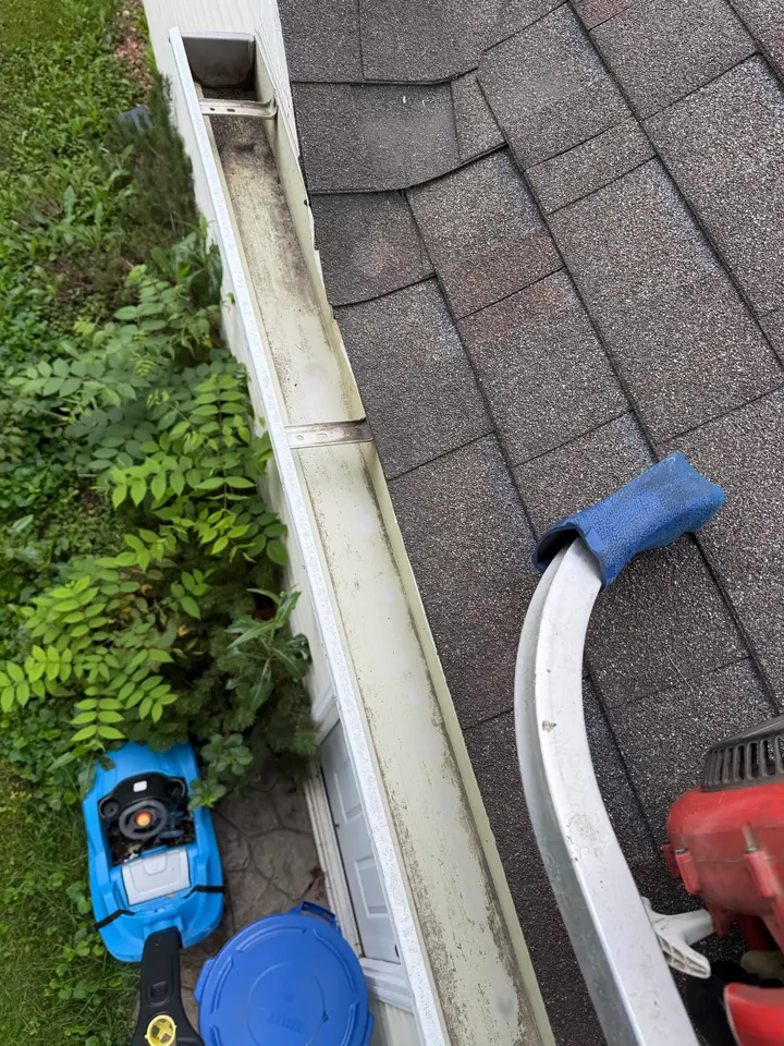 Clean, empty gutter after professional gutter cleaning, with a ladder standoff resting on the roof shingles
