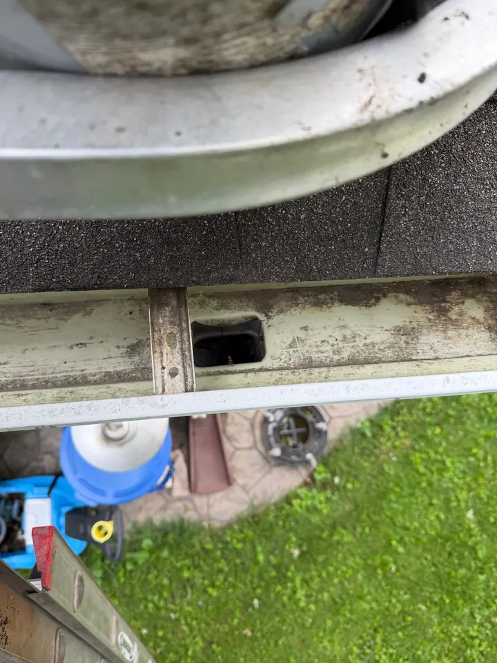 Cleared downspout opening inside a gutter after cleaning, with the debris gone and the drain hole open