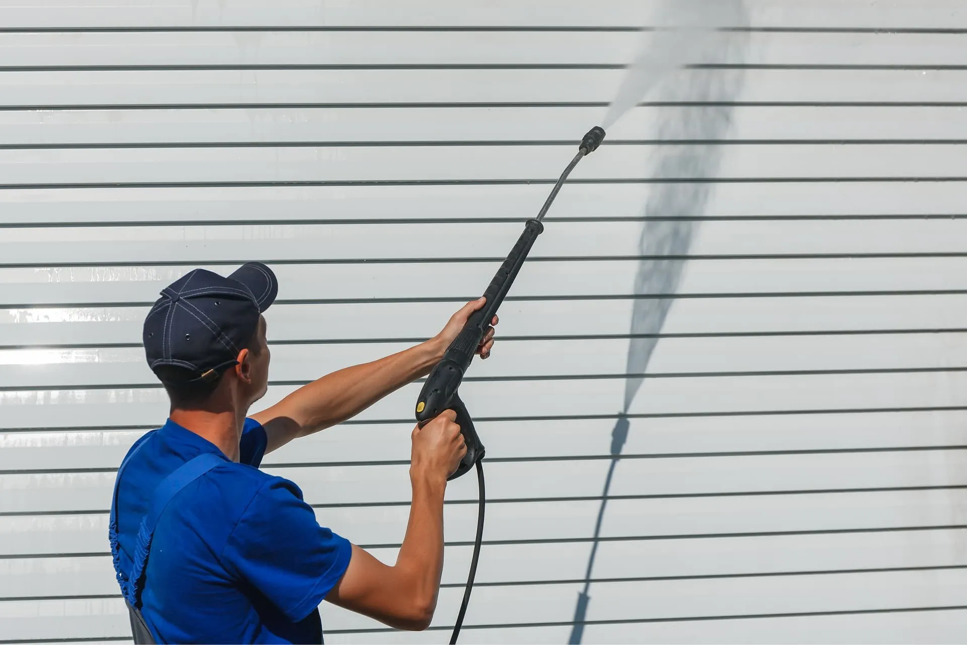 A Property Refresh worker in overalls power washing white house siding